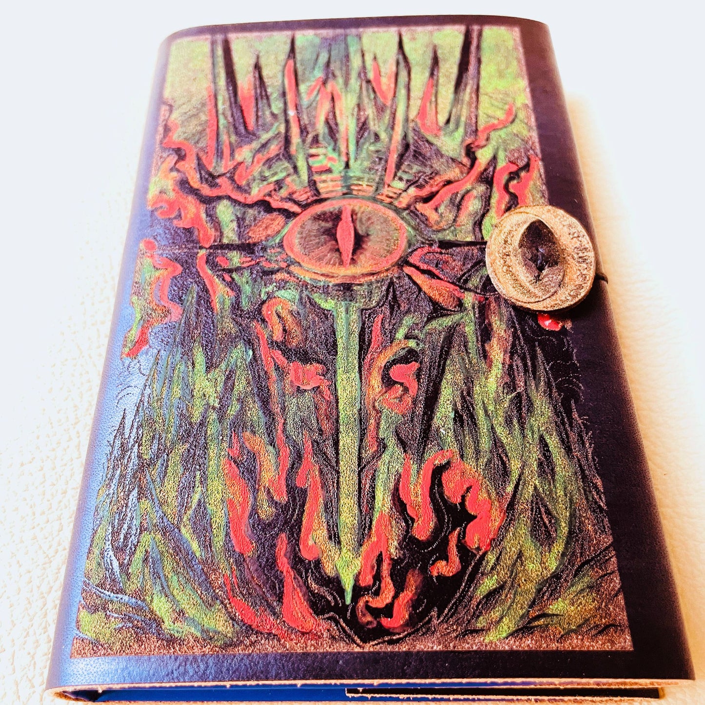 SteamVoyage - copertina in cuoio tinto di nero per agenda A6 con incisione a laser della Torre di Sauron dipinta a mano con colori fluo e cordino per la chiusura ornato da due anelli del potere in cuoio dorato
