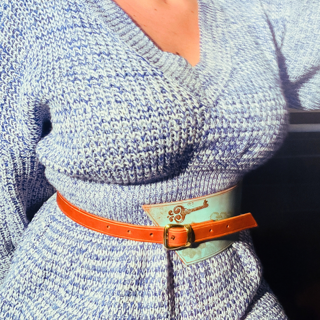 Cintura asimmetrica in cuoio dipinto con fantasia steampunk di ingranaggi, chiavi e catene. Sfondo azzurro e particolari oro, rame e argento. Cinturino laterale con doppia fibbia dorata