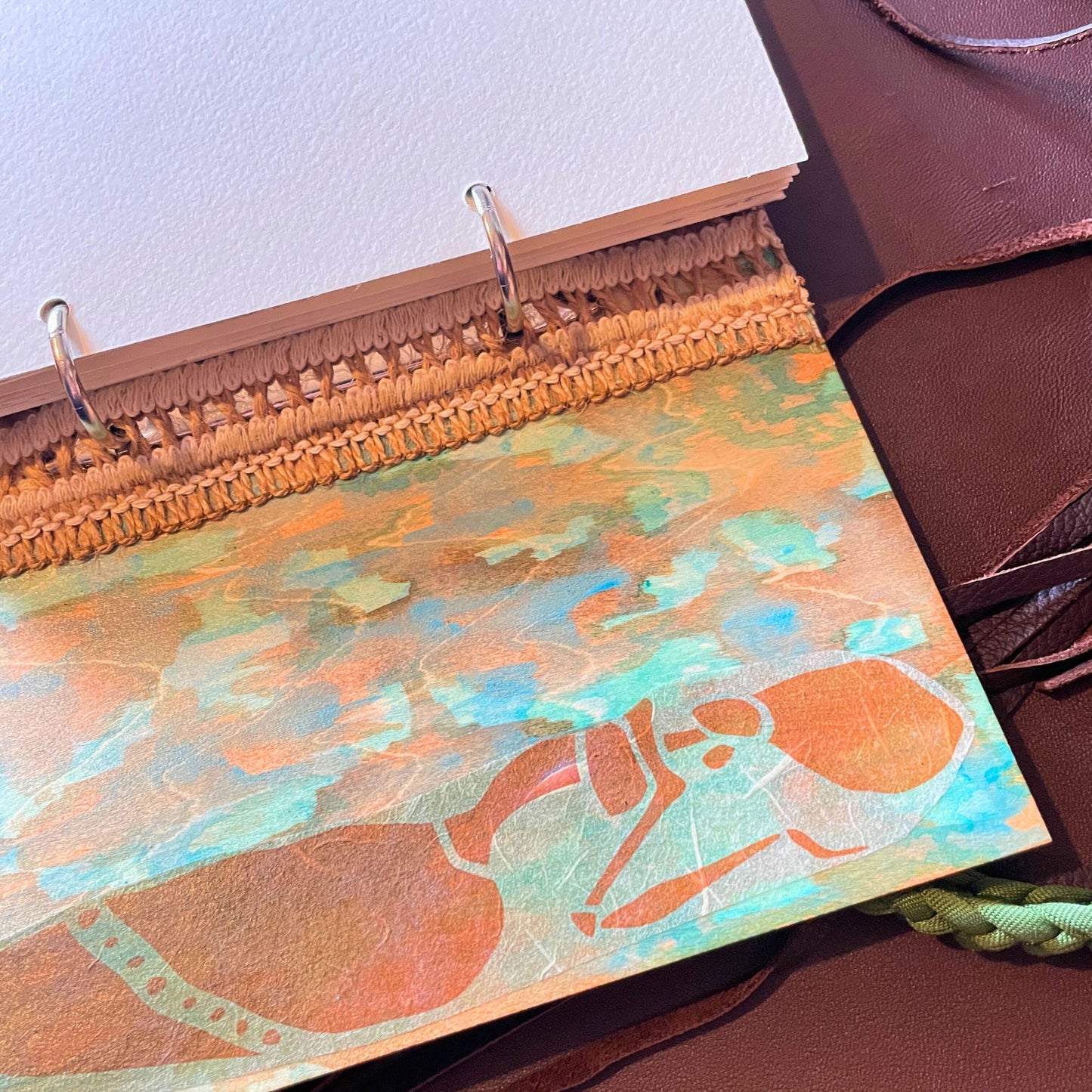 SteamVoyage - libro magico della sciamana in legno decorato con la tecnica del decoupage, rivestito in pelle marrone incisa al laser con fantasie africane dorate, con applicazioni in stoffa e perline e fettuccia per la chiusura in lycra lavorata all'uncinetto. All'interno, stampati su carta di pregio, si trovano preghiere e invocazioni, ricette per elisir magici e indicazioni per rituali arcani, oltre ad annotazioni personali della maga.