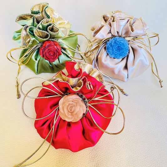 Tre bomboniere composte da sacchetto in raso rosso, bianco e verde con una spilla fissata sul fiocco. Sulla spilla è incastonata una rosa in resina epossidica: rosa su sacchetto rosso, rossa su sacchetto verde e blu su sacchetto bianco.