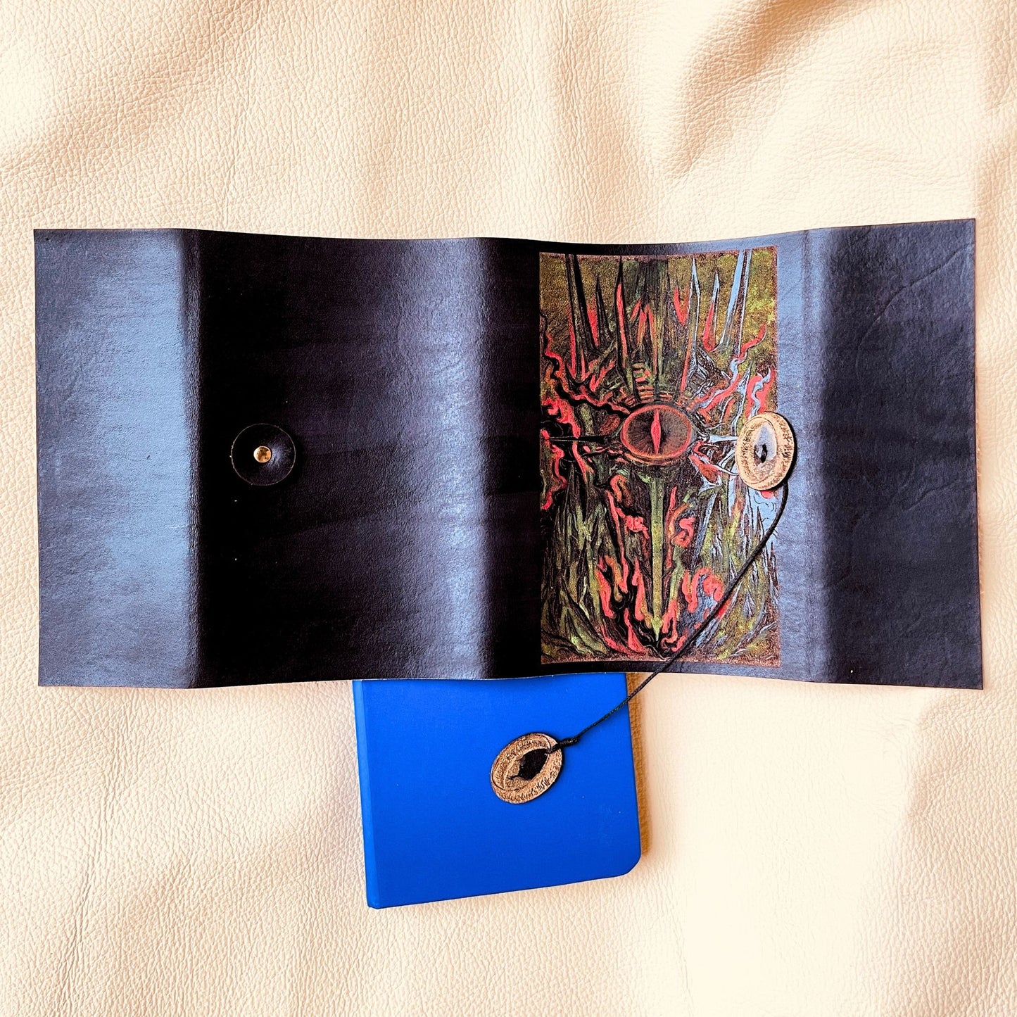 SteamVoyage - copertina in cuoio tinto di nero per agenda A6 con incisione a laser della Torre di Sauron dipinta a mano con colori fluo e cordino per la chiusura ornato da due anelli del potere in cuoio dorato