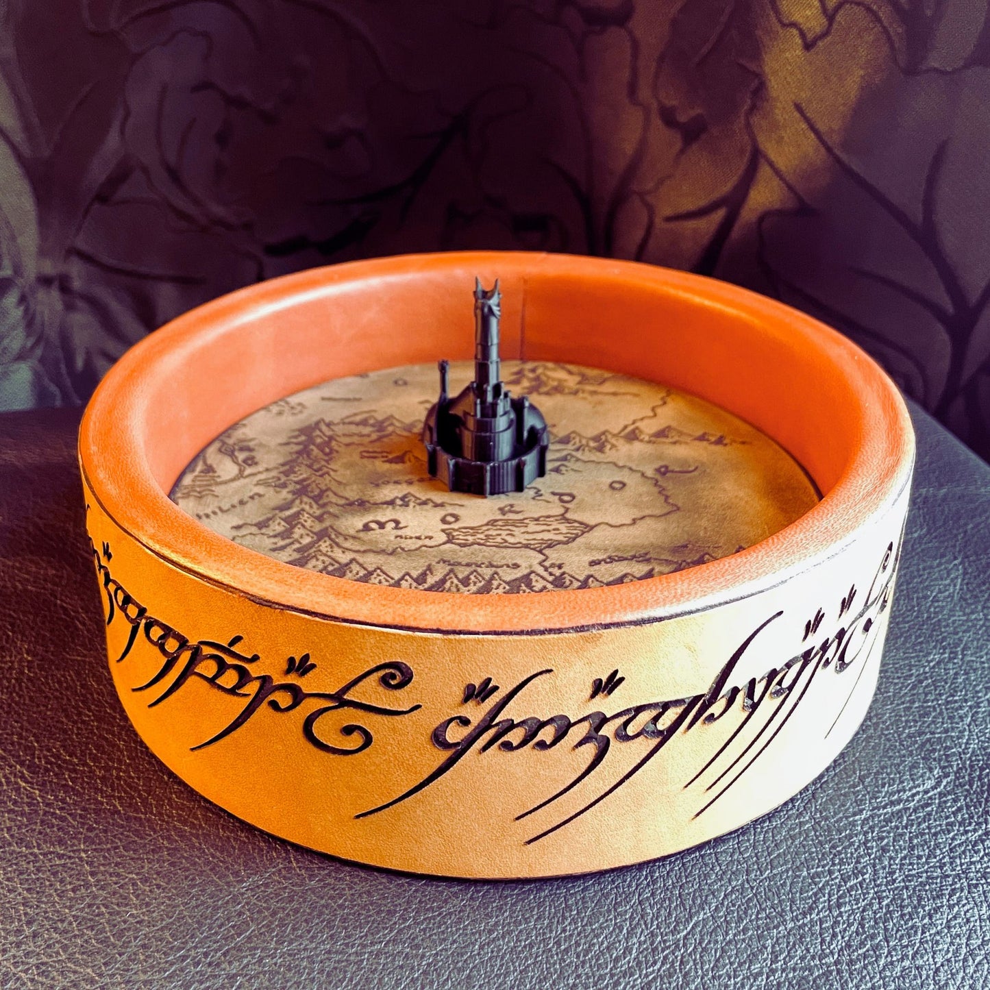 SteamVoyage - vassoio lancia dadi Torre di Sauron in cuoio e legno con incisione a laser della Mappa della Terra di Mezzo e Torre di Sauron in 3d; sul bordo del vassoio lancia dadi è presente l'incisione in elfico sull'Anello del Potere e il fondo nasconde una power bank in grado di illuminare la scritta dell'anello grazie ad un telecomando
