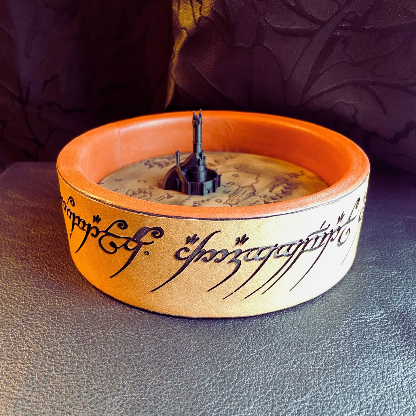SteamVoyage - vassoio lancia dadi Torre di Sauron in cuoio e legno con incisione a laser della Mappa della Terra di Mezzo e Torre di Sauron in 3d; sul bordo del vassoio lancia dadi è presente l'incisione in elfico sull'Anello del Potere e il fondo nasconde una power bank in grado di illuminare la scritta dell'anello grazie ad un telecomando