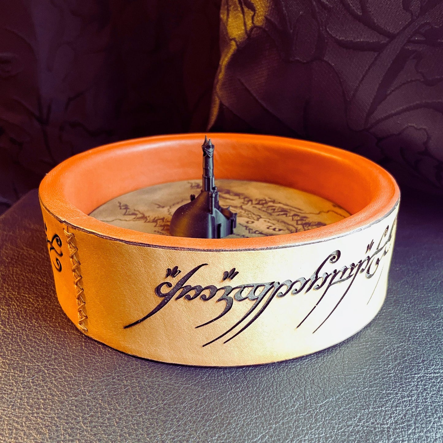 SteamVoyage - vassoio lancia dadi Torre di Sauron in cuoio e legno con incisione a laser della Mappa della Terra di Mezzo e Torre di Sauron in 3d; sul bordo del vassoio lancia dadi è presente l'incisione in elfico sull'Anello del Potere e il fondo nasconde una power bank in grado di illuminare la scritta dell'anello grazie ad un telecomando