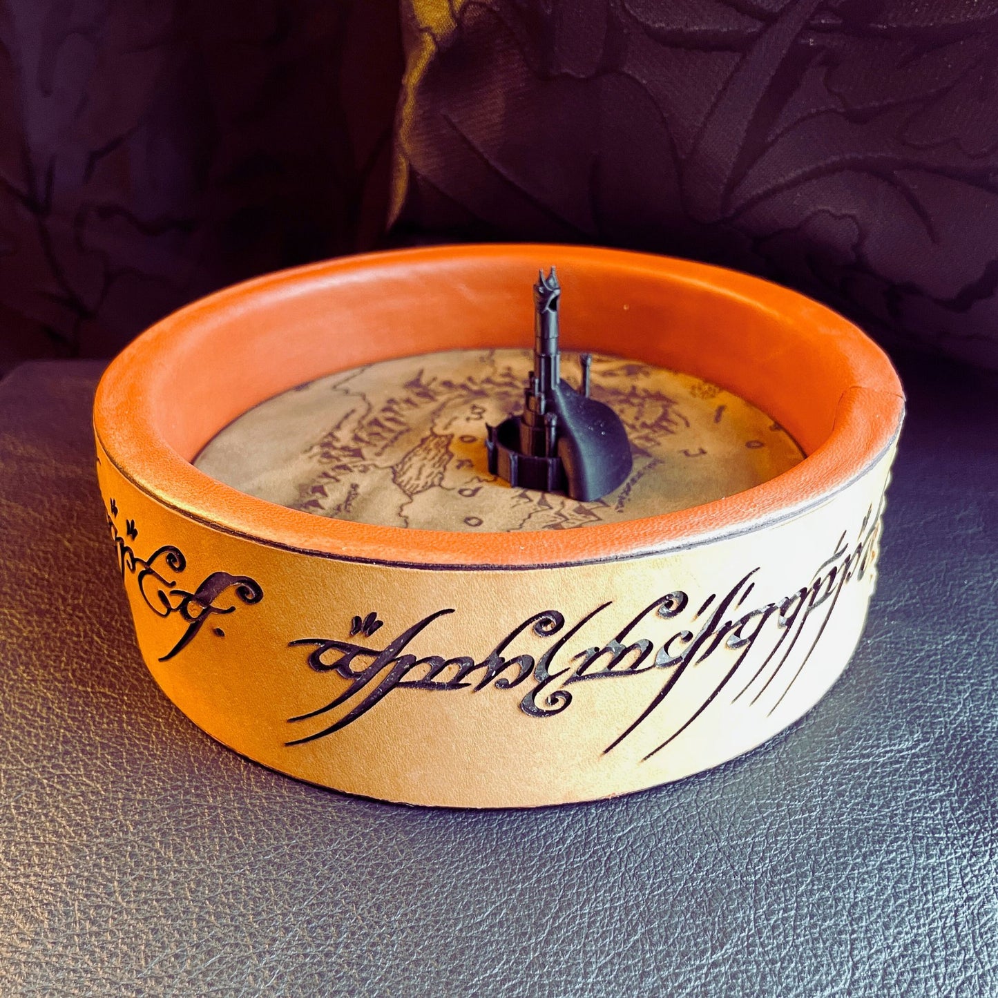 SteamVoyage - vassoio lancia dadi Torre di Sauron in cuoio e legno con incisione a laser della Mappa della Terra di Mezzo e Torre di Sauron in 3d; sul bordo del vassoio lancia dadi è presente l'incisione in elfico sull'Anello del Potere e il fondo nasconde una power bank in grado di illuminare la scritta dell'anello grazie ad un telecomando
