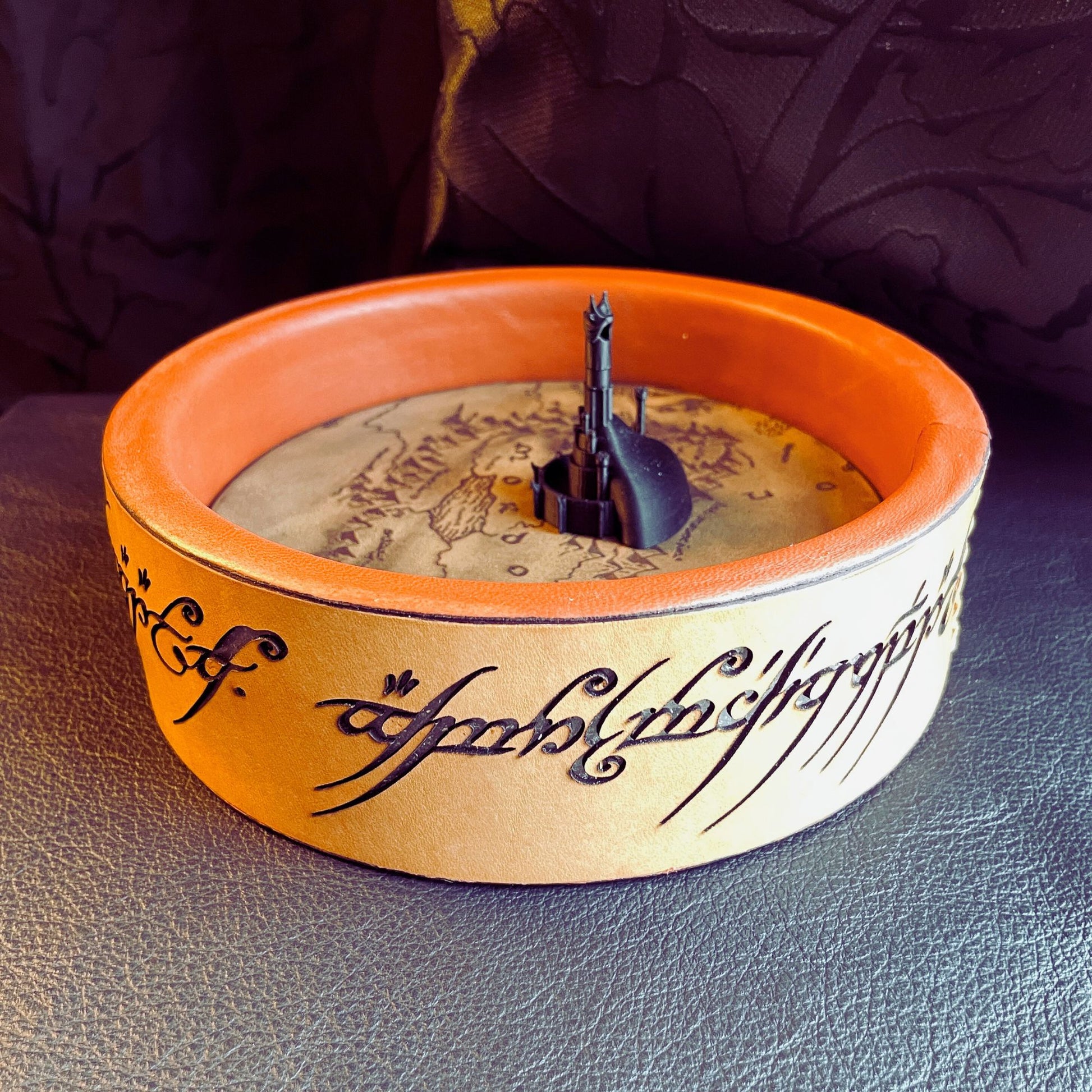 SteamVoyage - vassoio lancia dadi Torre di Sauron in cuoio e legno con incisione a laser della Mappa della Terra di Mezzo e Torre di Sauron in 3d; sul bordo del vassoio lancia dadi è presente l'incisione in elfico sull'Anello del Potere e il fondo nasconde una power bank in grado di illuminare la scritta dell'anello grazie ad un telecomando