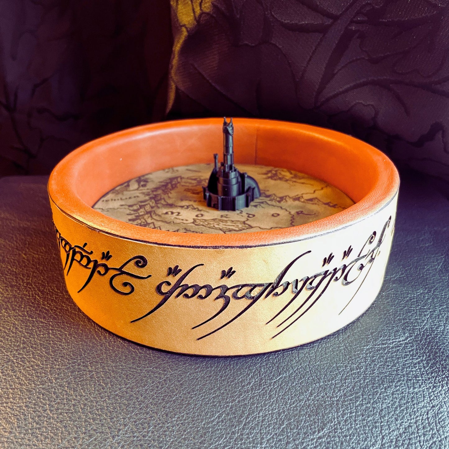 SteamVoyage - vassoio lancia dadi Torre di Sauron in cuoio e legno con incisione a laser della Mappa della Terra di Mezzo e Torre di Sauron in 3d; sul bordo del vassoio lancia dadi è presente l'incisione in elfico sull'Anello del Potere e il fondo nasconde una power bank in grado di illuminare la scritta dell'anello grazie ad un telecomando