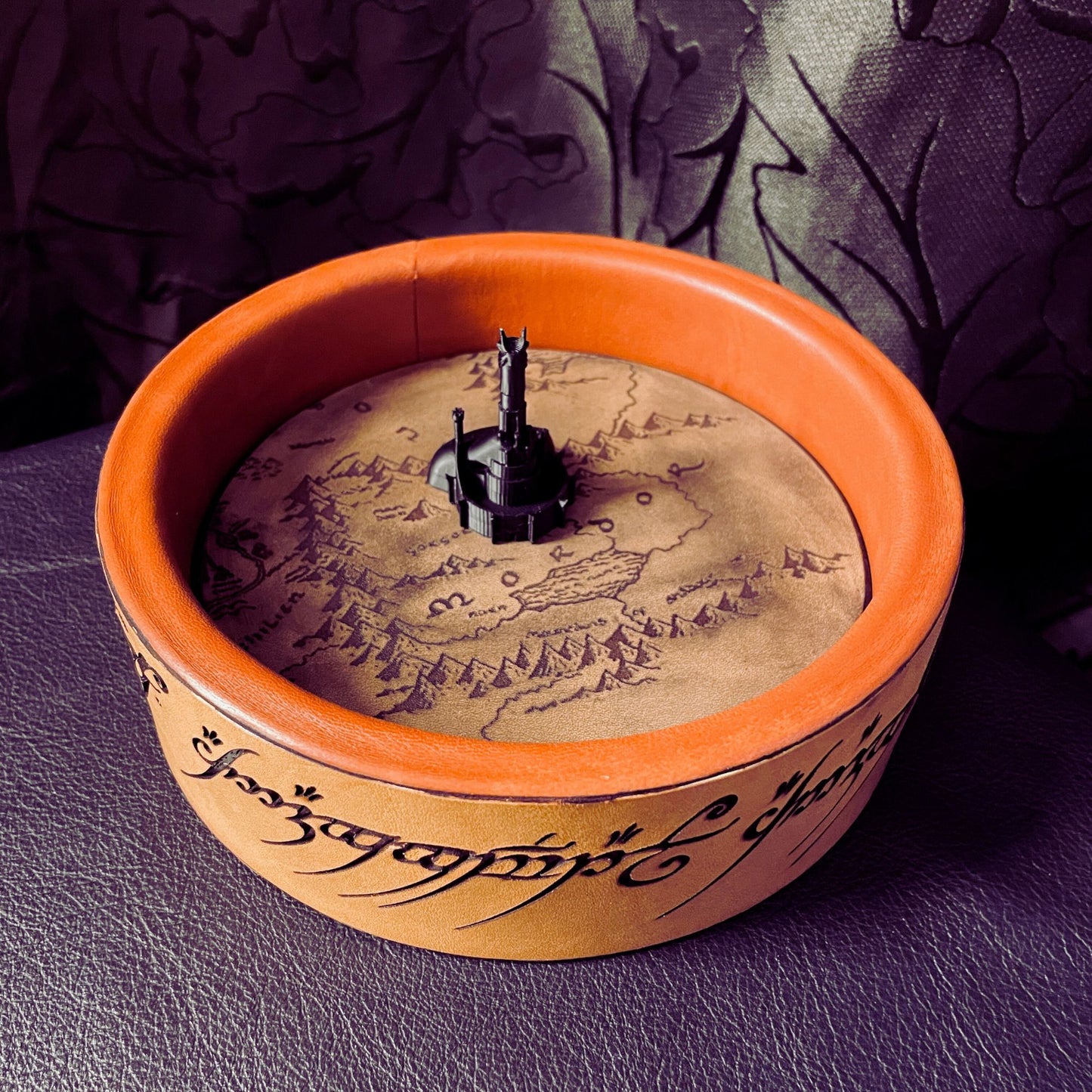 SteamVoyage - vassoio lancia dadi Torre di Sauron in cuoio e legno con incisione a laser della Mappa della Terra di Mezzo e Torre di Sauron in 3d; sul bordo del vassoio lancia dadi è presente l'incisione in elfico sull'Anello del Potere e il fondo nasconde una power bank in grado di illuminare la scritta dell'anello grazie ad un telecomando