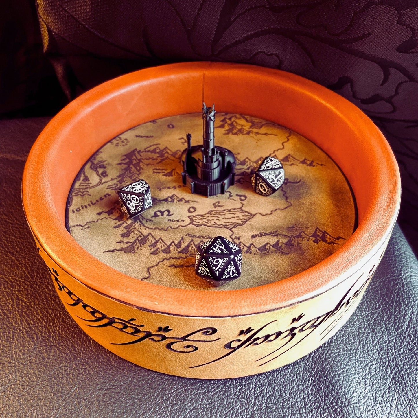 SteamVoyage - vassoio lancia dadi Torre di Sauron in cuoio e legno con incisione a laser della Mappa della Terra di Mezzo e Torre di Sauron in 3d; sul bordo del vassoio lancia dadi è presente l'incisione in elfico sull'Anello del Potere e il fondo nasconde una power bank in grado di illuminare la scritta dell'anello grazie ad un telecomando