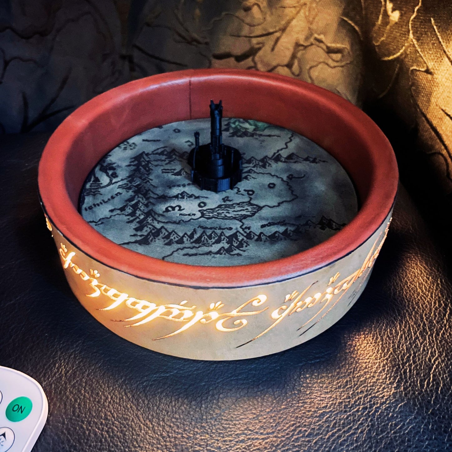 SteamVoyage - vassoio lancia dadi Torre di Sauron in cuoio e legno con incisione a laser della Mappa della Terra di Mezzo e Torre di Sauron in 3d; sul bordo del vassoio lancia dadi è presente l'incisione in elfico sull'Anello del Potere e il fondo nasconde una power bank in grado di illuminare la scritta dell'anello grazie ad un telecomando