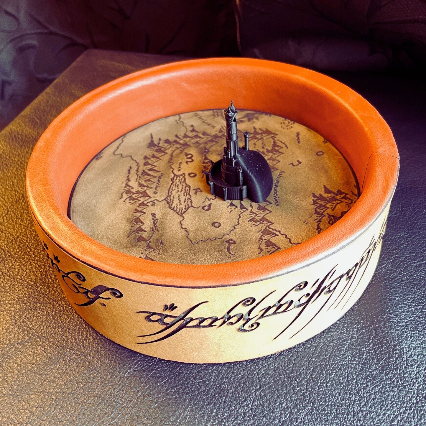 SteamVoyage - vassoio lancia dadi Torre di Sauron in cuoio e legno con incisione a laser della Mappa della Terra di Mezzo e Torre di Sauron in 3d; sul bordo del vassoio lancia dadi è presente l'incisione in elfico sull'Anello del Potere e il fondo nasconde una power bank in grado di illuminare la scritta dell'anello grazie ad un telecomando