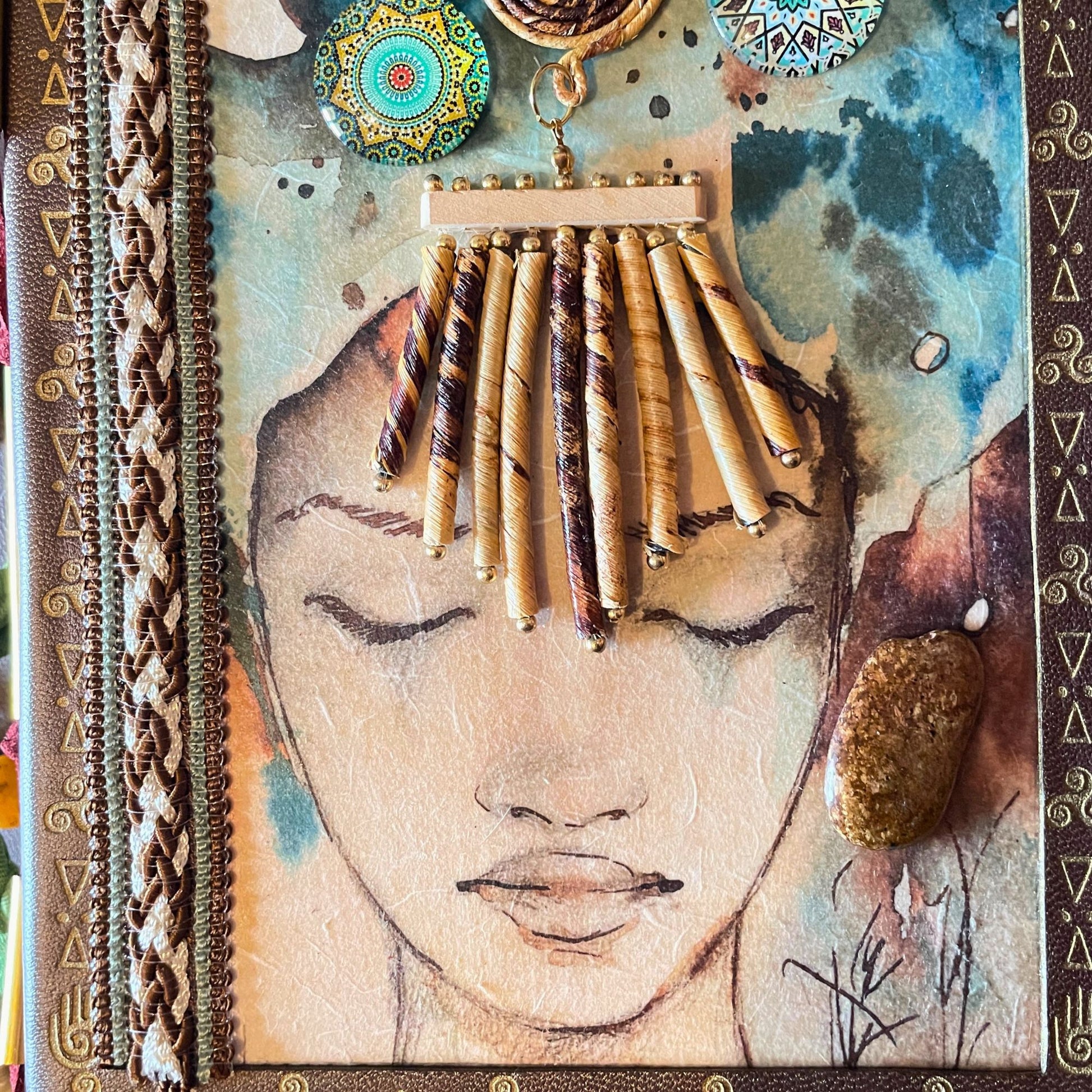 SteamVoyage - libro magico della sciamana in legno decorato con la tecnica del decoupage, rivestito in pelle marrone incisa al laser con fantasie africane dorate, con applicazioni in stoffa e perline e fettuccia per la chiusura in lycra lavorata all'uncinetto. All'interno, stampati su carta di pregio, si trovano preghiere e invocazioni, ricette per elisir magici e indicazioni per rituali arcani, oltre ad annotazioni personali della maga.