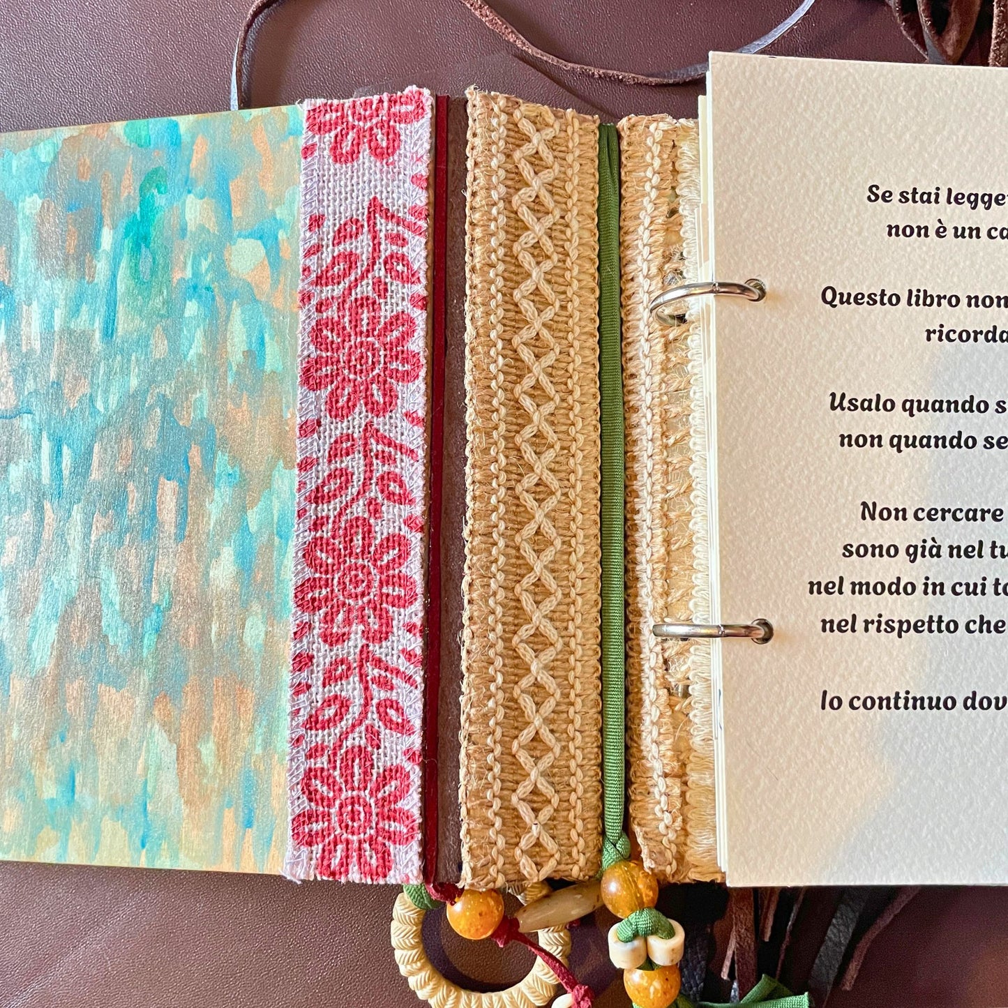 SteamVoyage - libro magico della sciamana in legno decorato con la tecnica del decoupage, rivestito in pelle marrone incisa al laser con fantasie africane dorate, con applicazioni in stoffa e perline e fettuccia per la chiusura in lycra lavorata all'uncinetto. All'interno, stampati su carta di pregio, si trovano preghiere e invocazioni, ricette per elisir magici e indicazioni per rituali arcani, oltre ad annotazioni personali della maga.