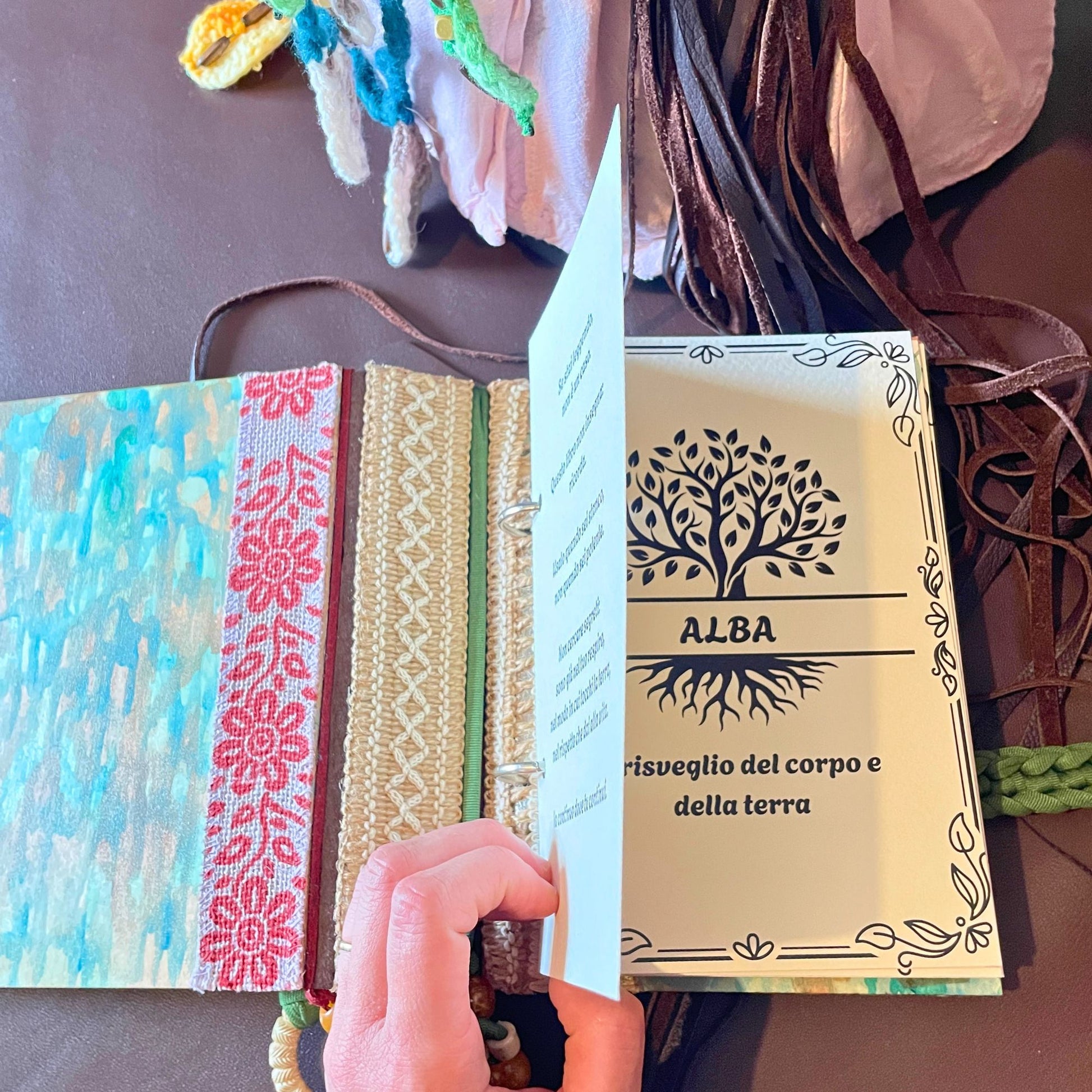 SteamVoyage - libro magico della sciamana in legno decorato con la tecnica del decoupage, rivestito in pelle marrone incisa al laser con fantasie africane dorate, con applicazioni in stoffa e perline e fettuccia per la chiusura in lycra lavorata all'uncinetto. All'interno, stampati su carta di pregio, si trovano preghiere e invocazioni, ricette per elisir magici e indicazioni per rituali arcani, oltre ad annotazioni personali della maga.