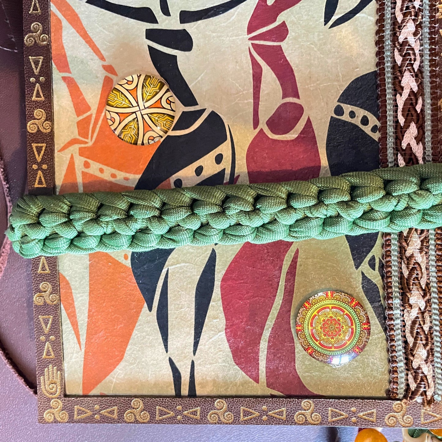 SteamVoyage - libro magico della sciamana in legno decorato con la tecnica del decoupage, rivestito in pelle marrone incisa al laser con fantasie africane dorate, con applicazioni in stoffa e perline e fettuccia per la chiusura in lycra lavorata all'uncinetto. All'interno, stampati su carta di pregio, si trovano preghiere e invocazioni, ricette per elisir magici e indicazioni per rituali arcani, oltre ad annotazioni personali della maga.