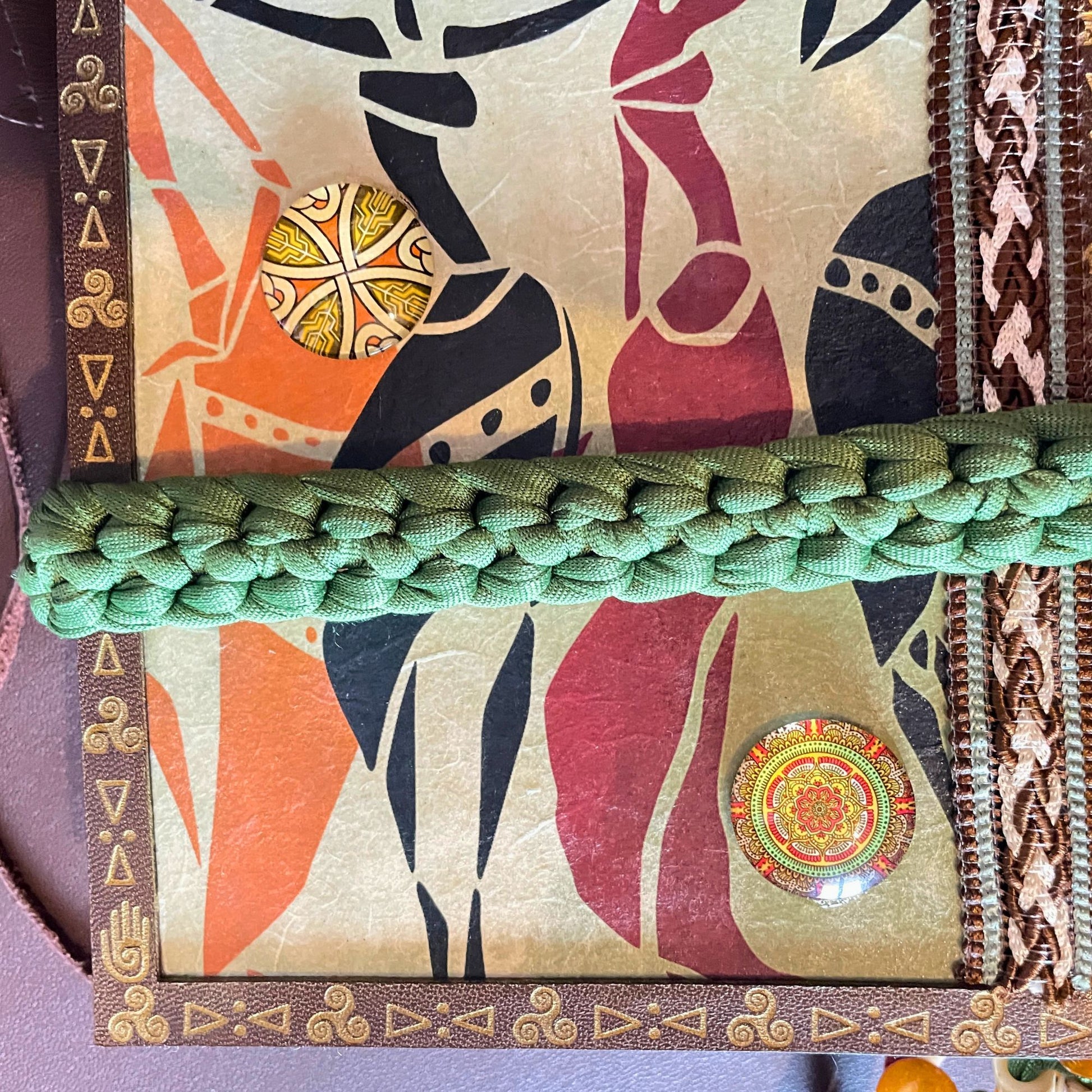 SteamVoyage - libro magico della sciamana in legno decorato con la tecnica del decoupage, rivestito in pelle marrone incisa al laser con fantasie africane dorate, con applicazioni in stoffa e perline e fettuccia per la chiusura in lycra lavorata all'uncinetto. All'interno, stampati su carta di pregio, si trovano preghiere e invocazioni, ricette per elisir magici e indicazioni per rituali arcani, oltre ad annotazioni personali della maga.