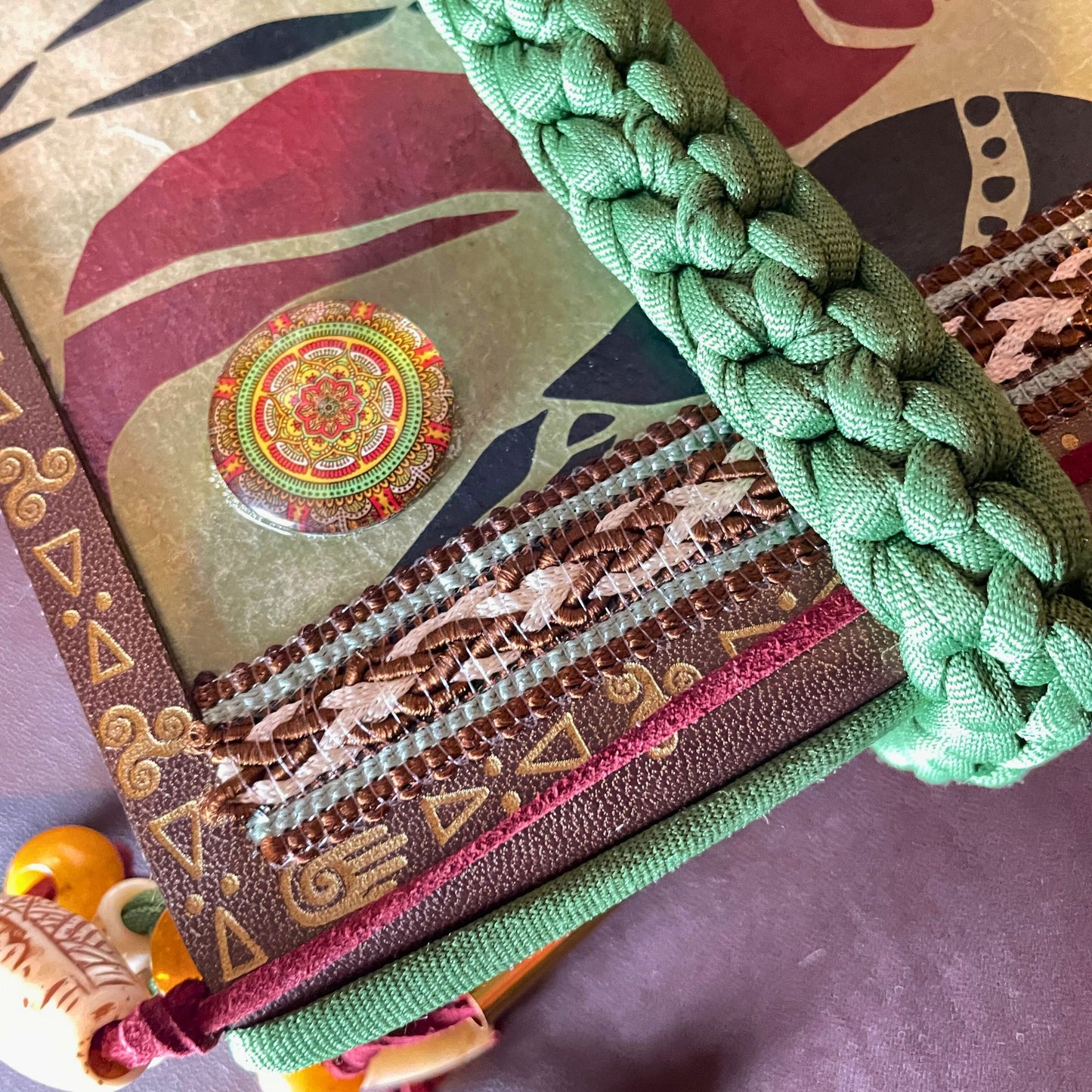 SteamVoyage - libro magico della sciamana in legno decorato con la tecnica del decoupage, rivestito in pelle marrone incisa al laser con fantasie africane dorate, con applicazioni in stoffa e perline e fettuccia per la chiusura in lycra lavorata all'uncinetto. All'interno, stampati su carta di pregio, si trovano preghiere e invocazioni, ricette per elisir magici e indicazioni per rituali arcani, oltre ad annotazioni personali della maga.