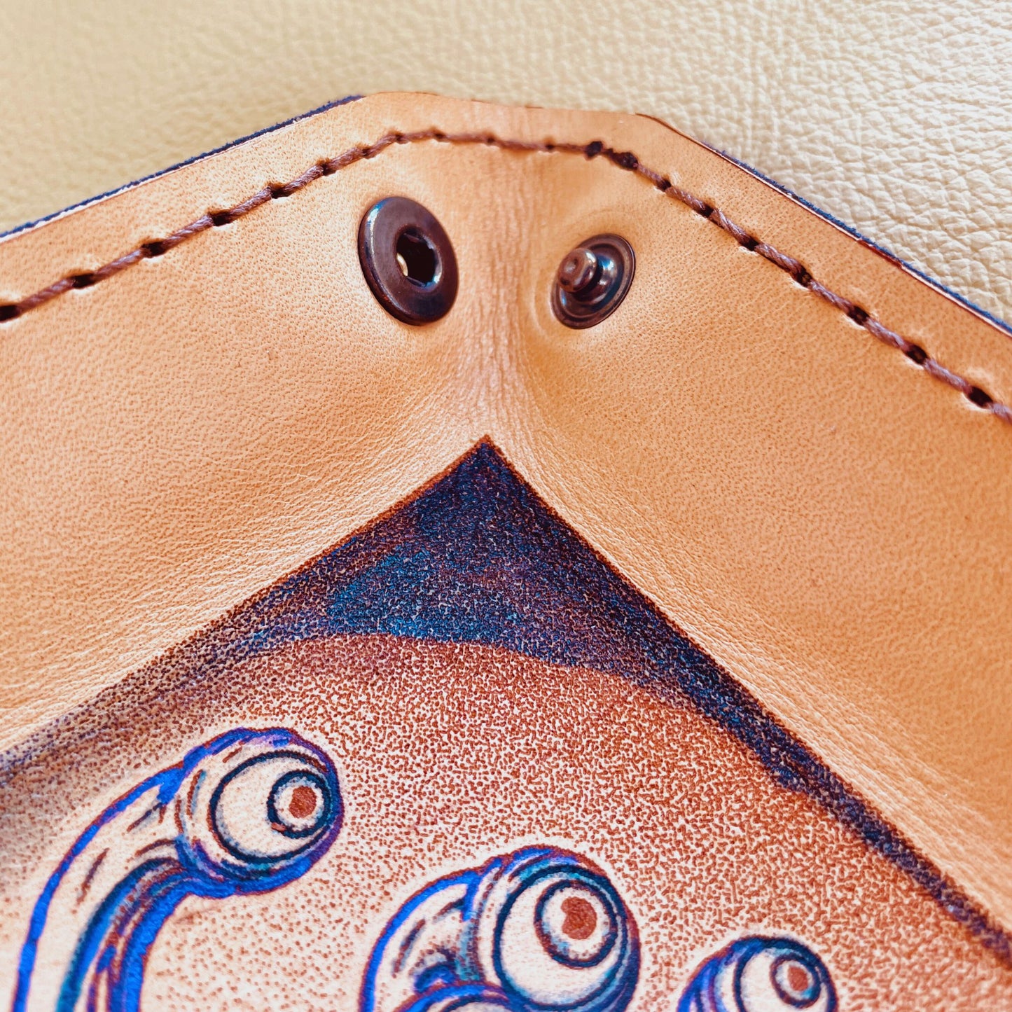 SteamVoyage - vassoio lancia dadi in cuoio dipinto a mano rivestito con pelle blu, dotato di quattro bottoni angolari per la chiusura e cucitura sul bordo. Il vassoio lancia dadi è decorato con l'immagine di un beholder, mostro tipico di Dungeons and dragons, dipinto con colori vivaci: viola e blu