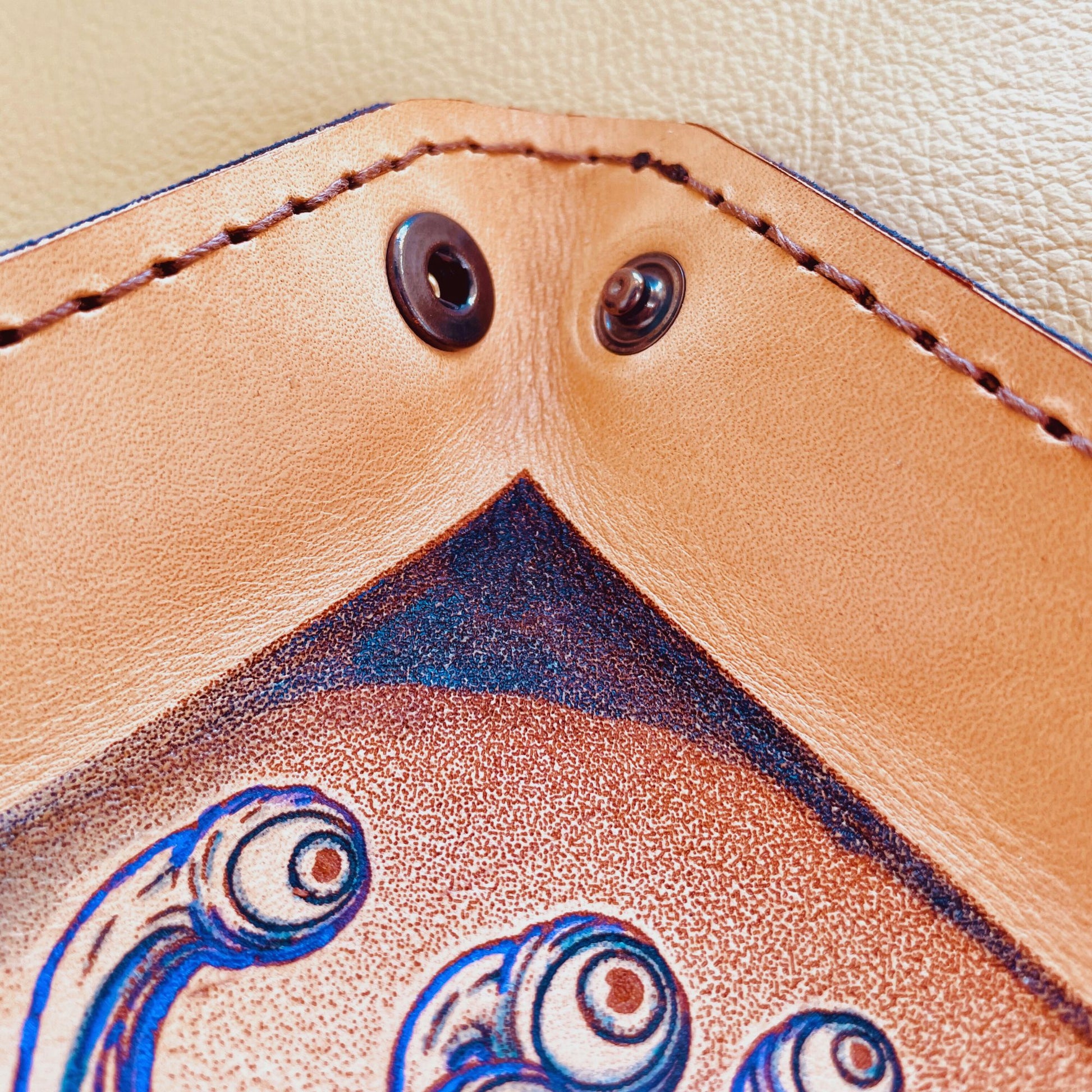 SteamVoyage - vassoio lancia dadi in cuoio dipinto a mano rivestito con pelle blu, dotato di quattro bottoni angolari per la chiusura e cucitura sul bordo. Il vassoio lancia dadi è decorato con l'immagine di un beholder, mostro tipico di Dungeons and dragons, dipinto con colori vivaci: viola e blu